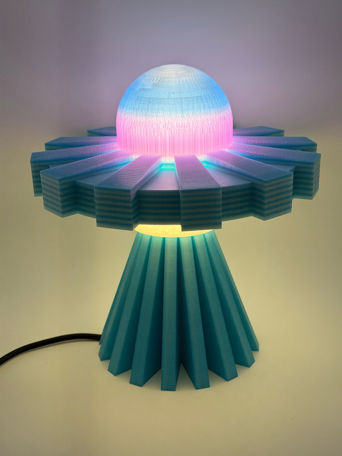 Retro UFO LED desk lamp switched on, dome glowing pink and blue with warm light beaming down onto the base